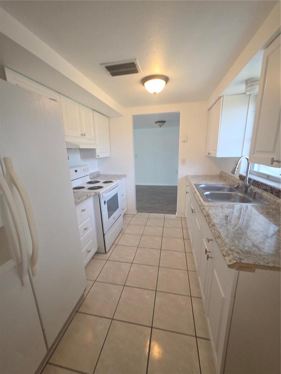 A galley kitchen features white cabinets, granite countertops, white appliances, and light-colored tile flooring — 1505 ROUNDTREE ROAD, HOLIDAY, FL