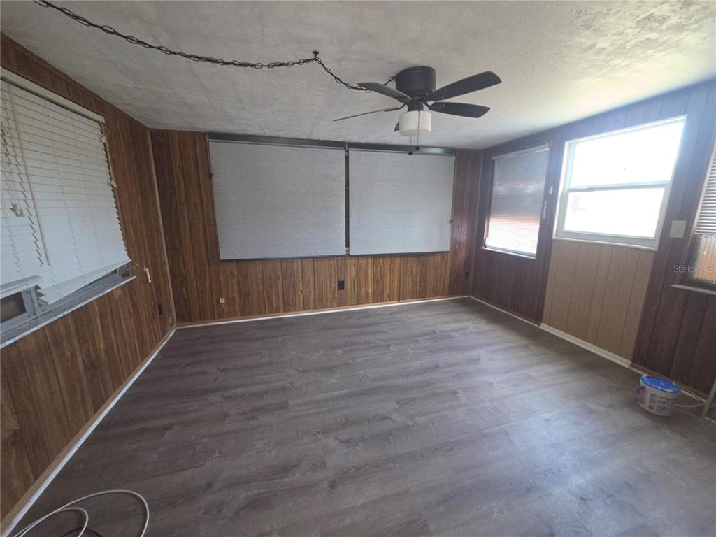 A room with dark wood paneling, grey wood-look flooring, and a ceiling fan — 1505 ROUNDTREE ROAD, HOLIDAY, FL