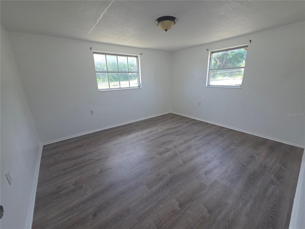 An empty room features white walls, wood-look flooring, two windows, and a ceiling light fixture — 1505 ROUNDTREE ROAD, HOLIDAY, FL