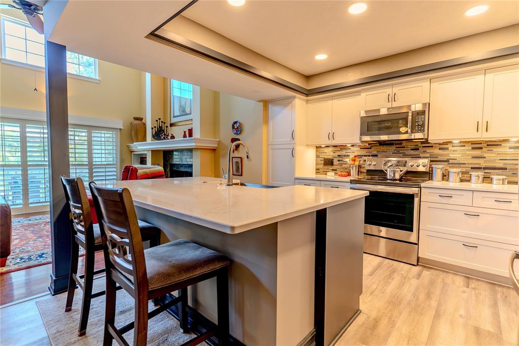 A kitchen features white cabinets, a quartz-topped island with seating, and a stainless steel stove — 14 BAYWOOD DRIVE, PALM HARBOR, FL