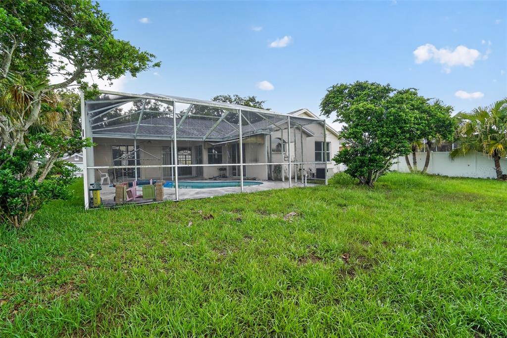 A backyard view of a house with a screened-in pool enclosure and surrounding lawn — 13126 PRESTWICK DRIVE, RIVERVIEW, FL