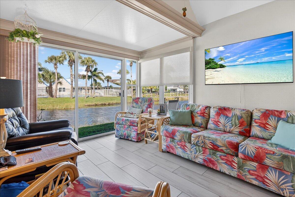 A sunroom features a floral sofa, wicker chairs, tile flooring, and a view of water — 1827 Aynsley Way # 4, Vero Beach FL 32966, VERO BEACH, FL