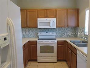 A kitchen features wood cabinets, a white stove, a microwave, and a blue tiled backsplash — 3903 45TH TERRACE W UNIT 104, BRADENTON, FL