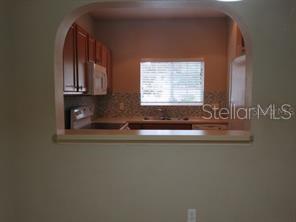 A kitchen viewed through an arched wall opening, featuring wooden cabinets and a window — 3903 45TH TERRACE W UNIT 104, BRADENTON, FL