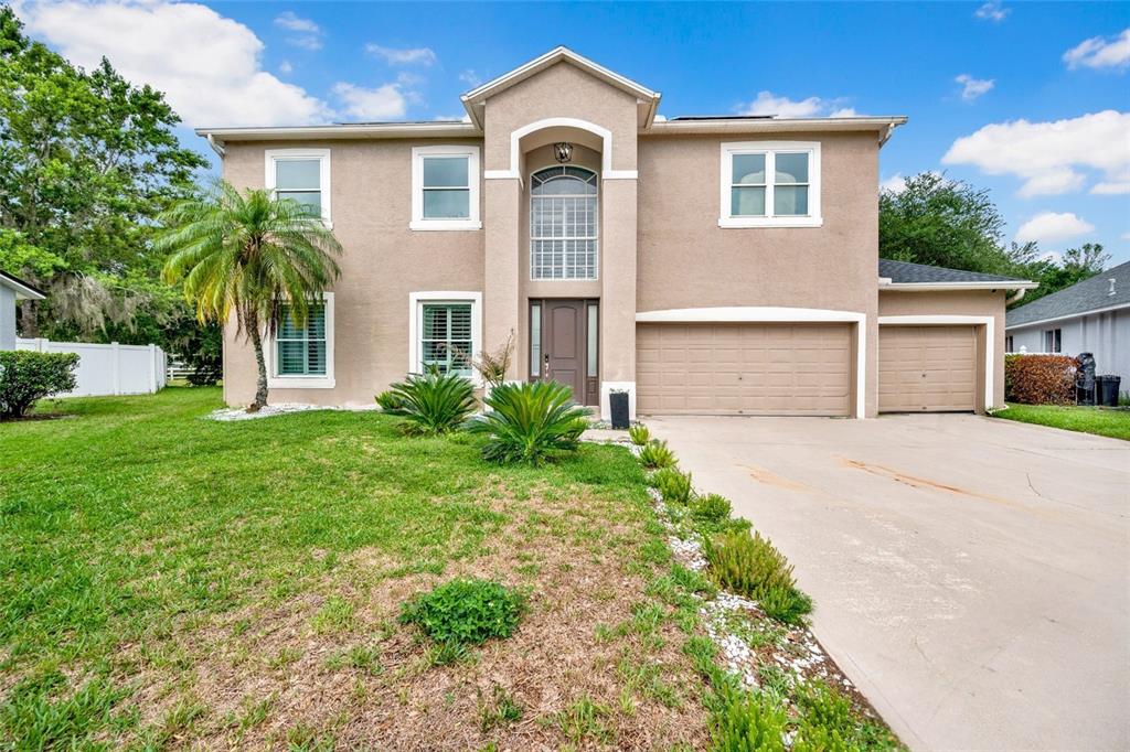 A two-story tan stucco house with a three-car garage and a front-facing palm tree — 3103 ASHMONTE DRIVE, LAND O LAKES, FL