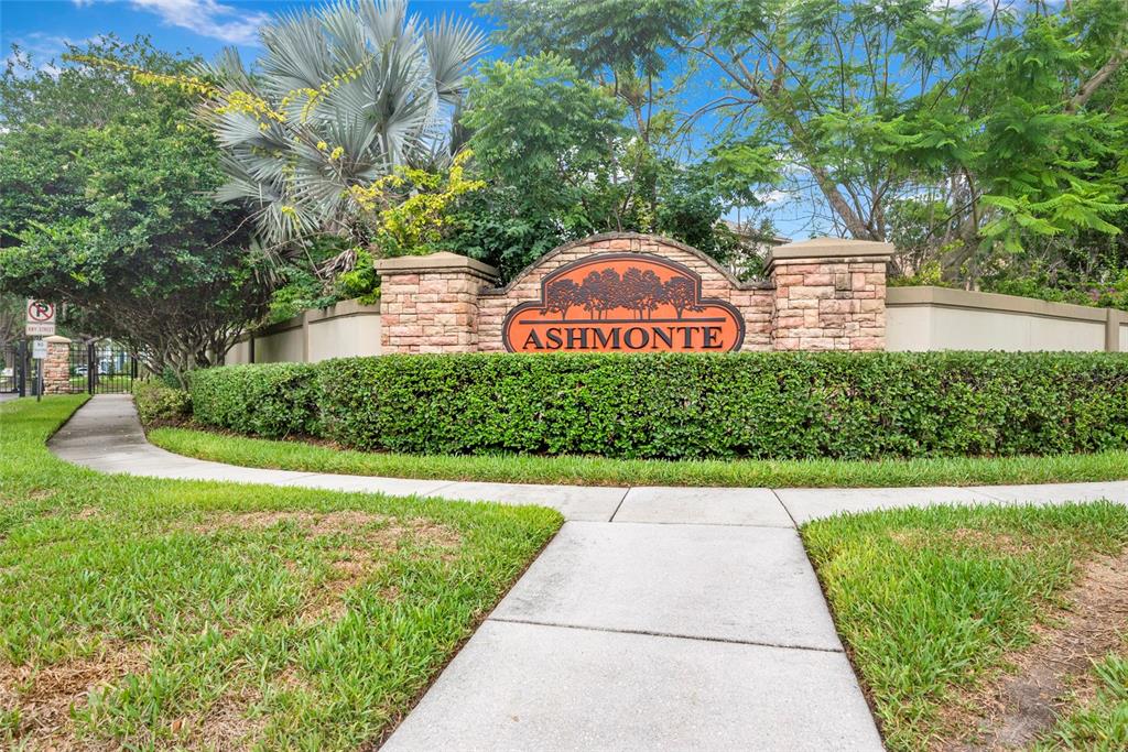 A stone monument sign for Ashmonte stands behind a manicured hedge and concrete sidewalk — 3103 ASHMONTE DRIVE, LAND O LAKES, FL