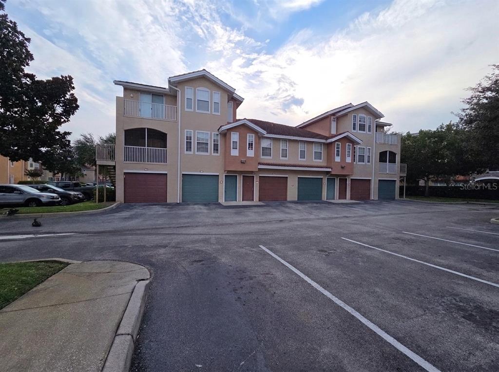 A multi-story apartment building features several garage doors and balconies under a cloudy sky — 12110 POPPY FIELD LANE UNIT 104, ORLANDO, FL