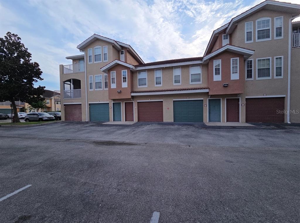 A multi-story residential building with several garage doors and balconies under a cloudy sky — 12110 POPPY FIELD LANE UNIT 104, ORLANDO, FL