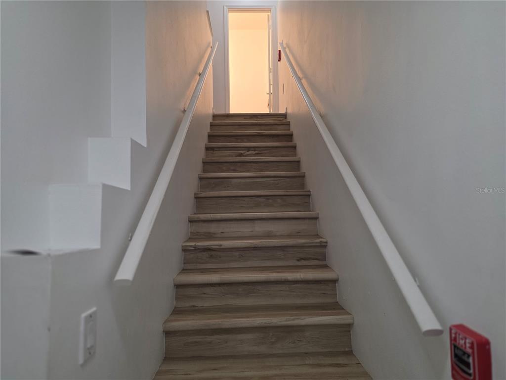 A straight staircase with wood-look steps and white handrails leads to an open doorway — 12110 POPPY FIELD LANE UNIT 104, ORLANDO, FL