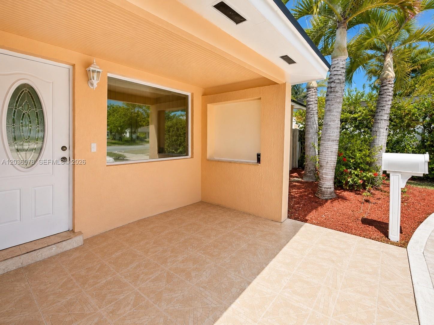 A covered front porch features tiled flooring, a white front door, and a recessed wall — 3327 Taft St, Hollywood FL 33021, HOLLYWOOD, FL