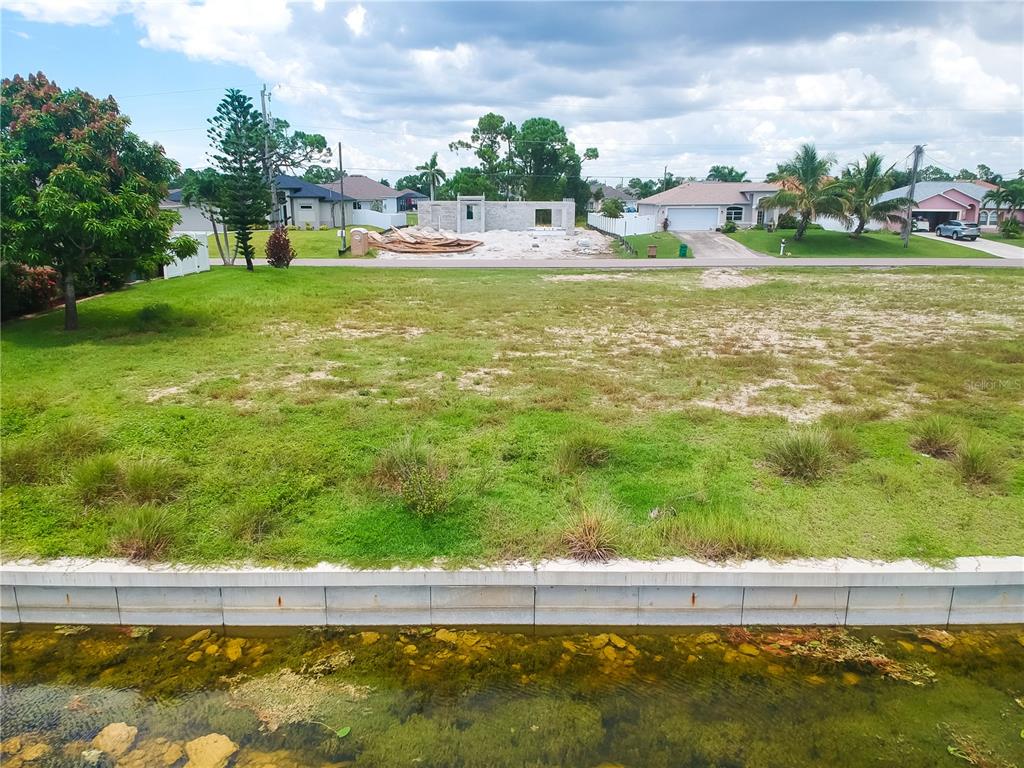 An elevated view shows a vacant grassy lot with a concrete seawall bordering a canal — 2614 NW 26TH TERRACE, CAPE CORAL, FL