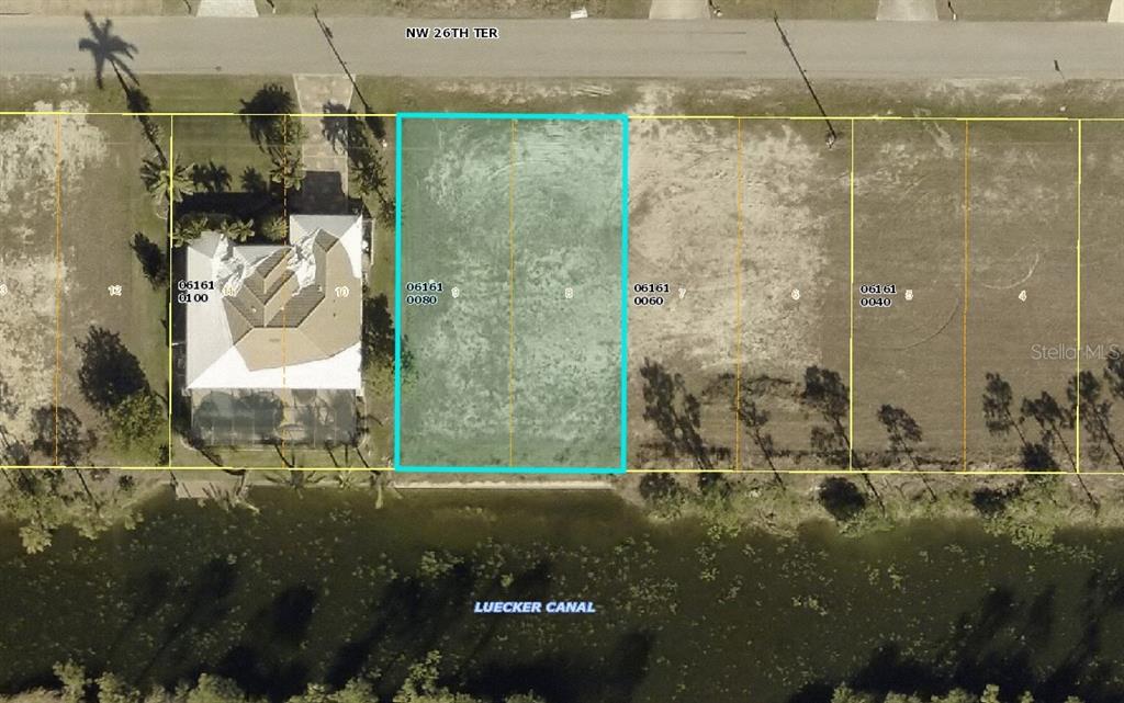 This is an aerial map showing a vacant residential lot highlighted in blue along a canal — 2614 NW 26TH TERRACE, CAPE CORAL, FL