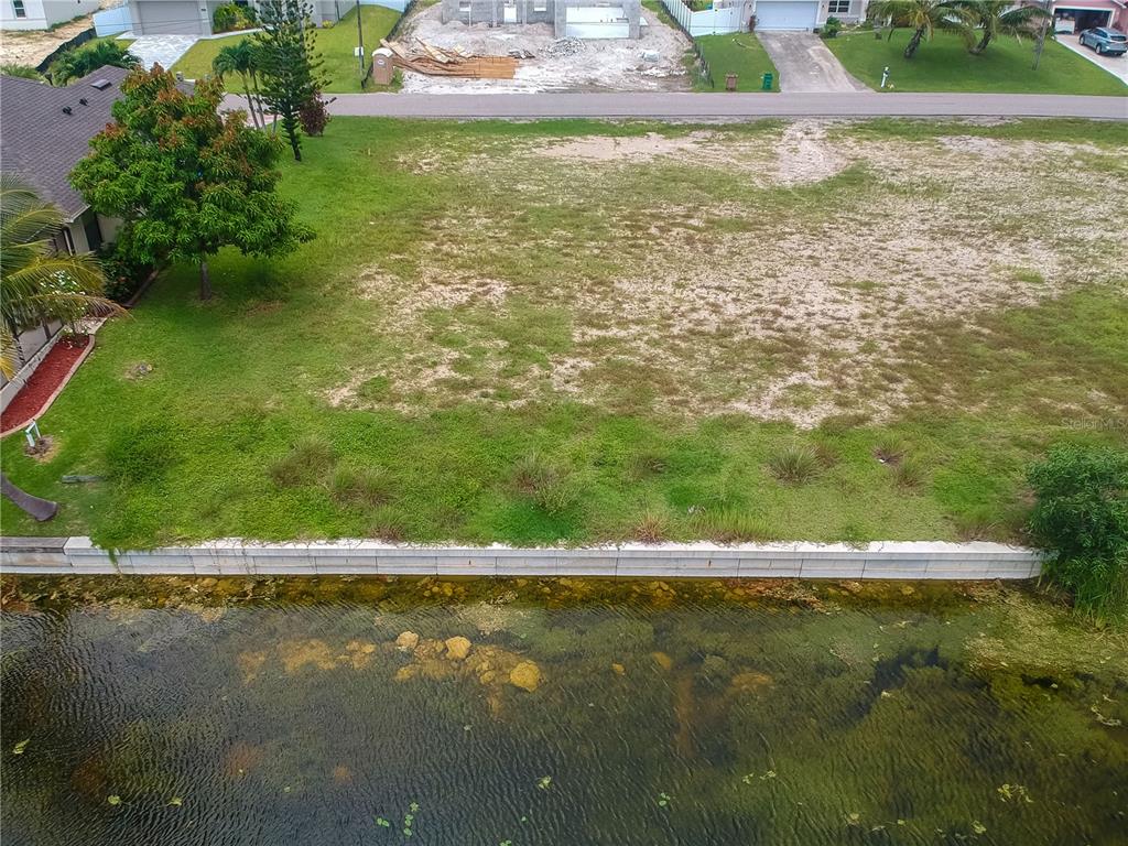 An aerial view of a vacant waterfront lot with a concrete seawall and grassy terrain — 2614 NW 26TH TERRACE, CAPE CORAL, FL