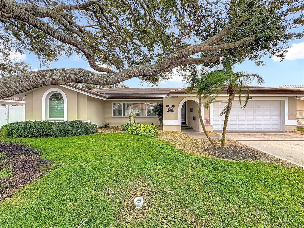 A single-story house with a large oak tree, a two-car garage, and a manicured lawn — 3828 48TH AVENUE S, ST PETERSBURG, FL