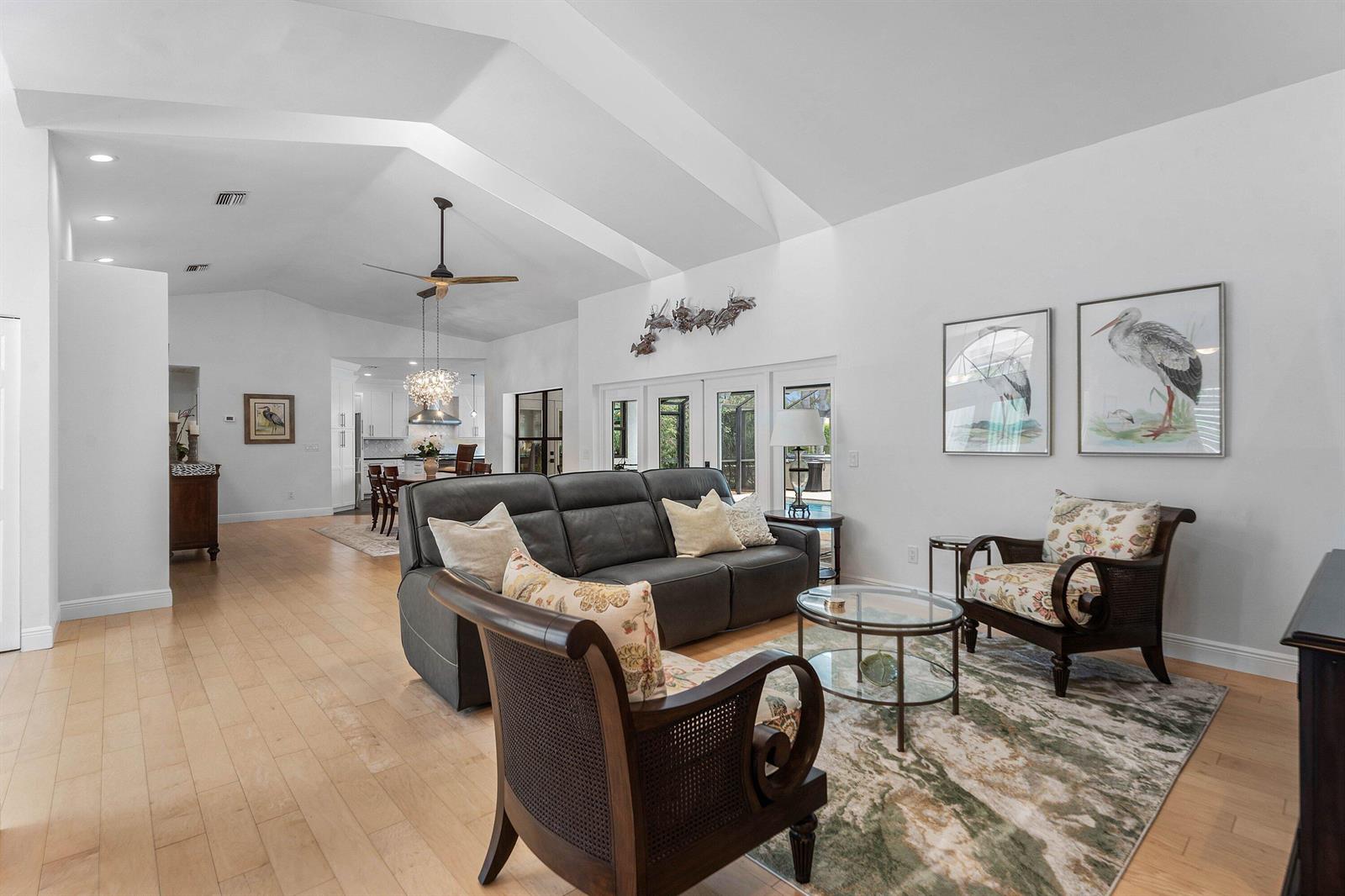 A living room with vaulted ceilings, light wood floors, a dark sofa, and two armchairs — 1488 SE Colony Way, Jupiter FL 33478, JUPITER, FL