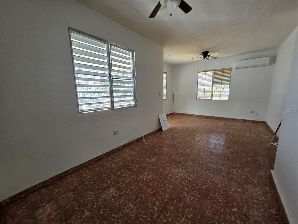 An empty room features tiled floors, white walls, two windows with blinds, and ceiling fans — 150 ROMAGUERA ST, MAYAGUEZ, PR
