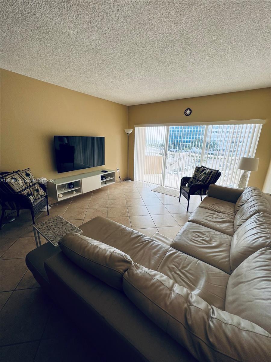 A living room features a large sectional sofa, a wall-mounted television, and a sliding glass door — 1950 S Ocean Dr # 4C, Hallandale Beach FL 33009, HALLANDALE BEACH, FL