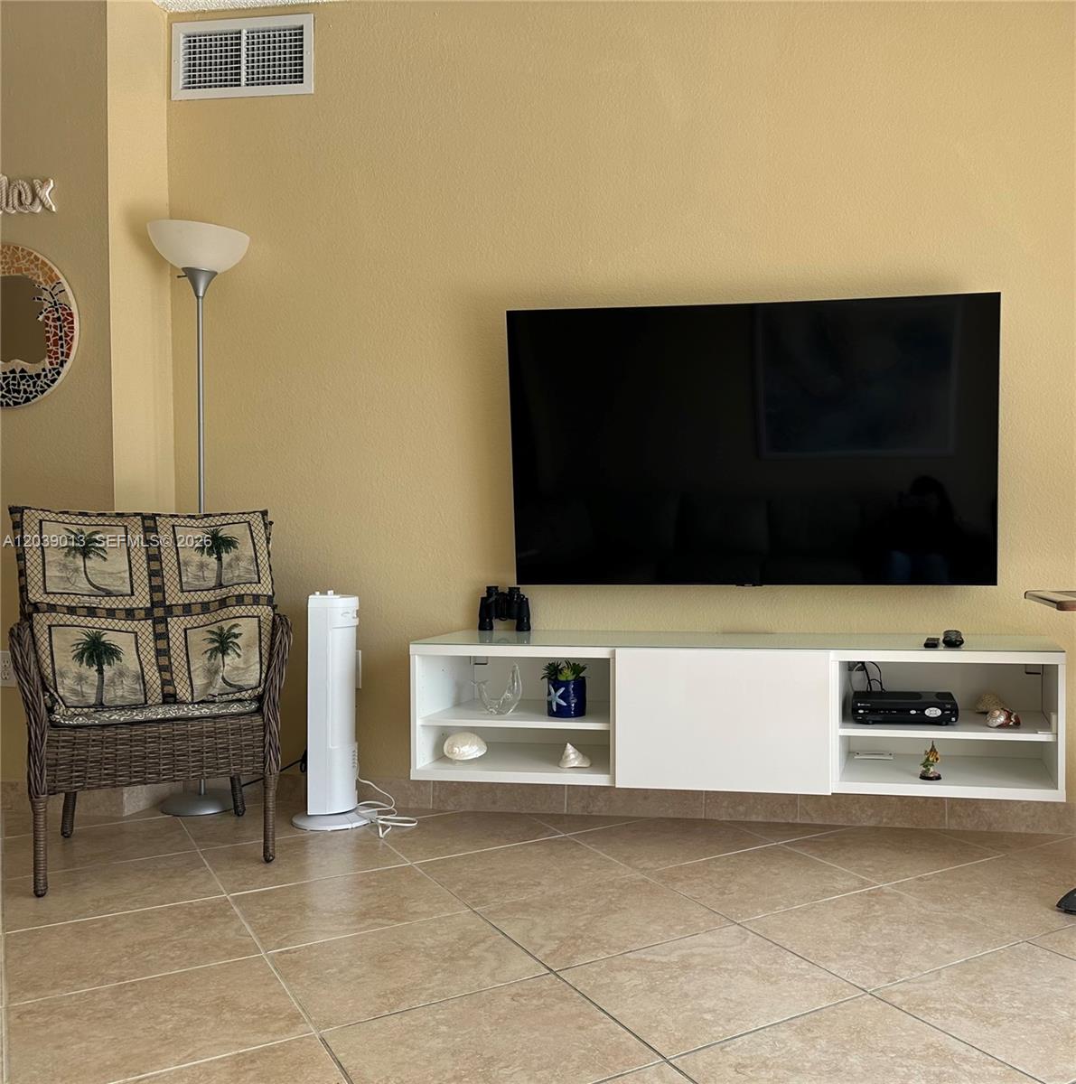 A living room features a wall-mounted television above a white media console and wicker chair — 1950 S Ocean Dr # 4C, Hallandale Beach FL 33009, HALLANDALE BEACH, FL