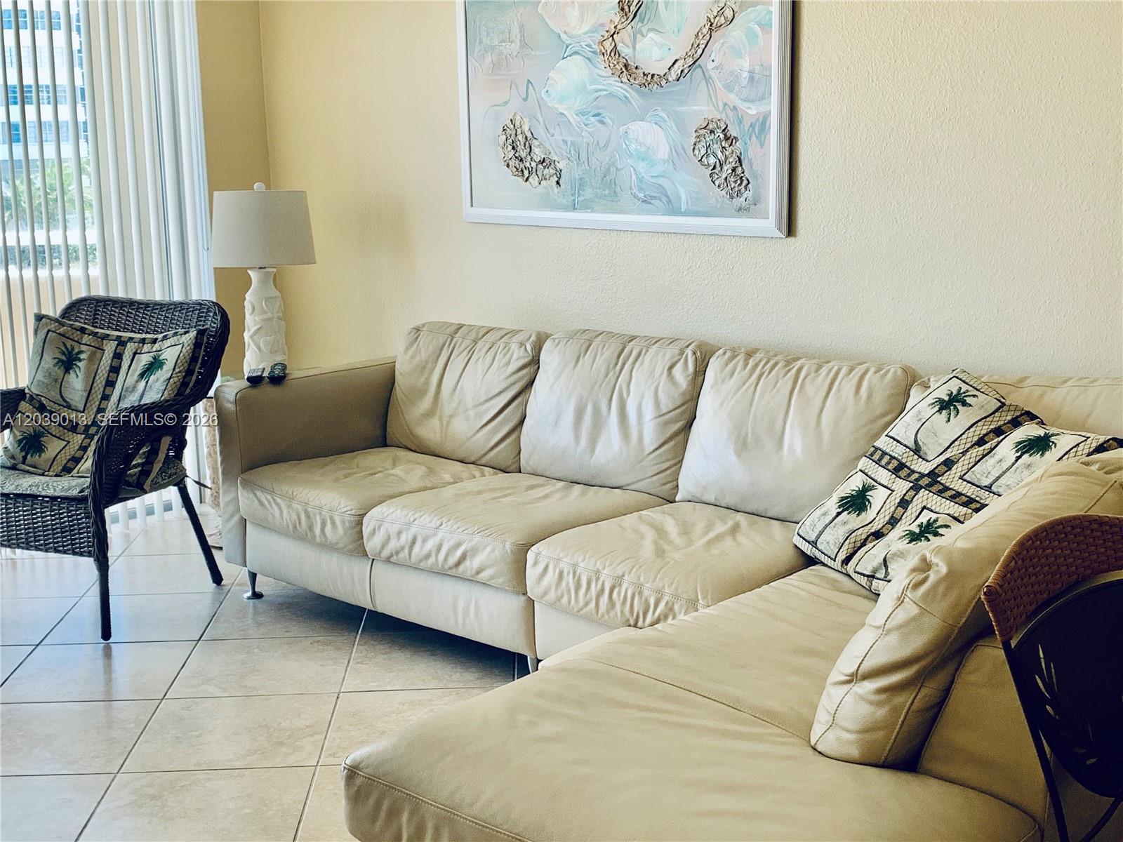 A living room features a beige leather sectional sofa, a wicker chair, and wall art — 1950 S Ocean Dr # 4C, Hallandale Beach FL 33009, HALLANDALE BEACH, FL