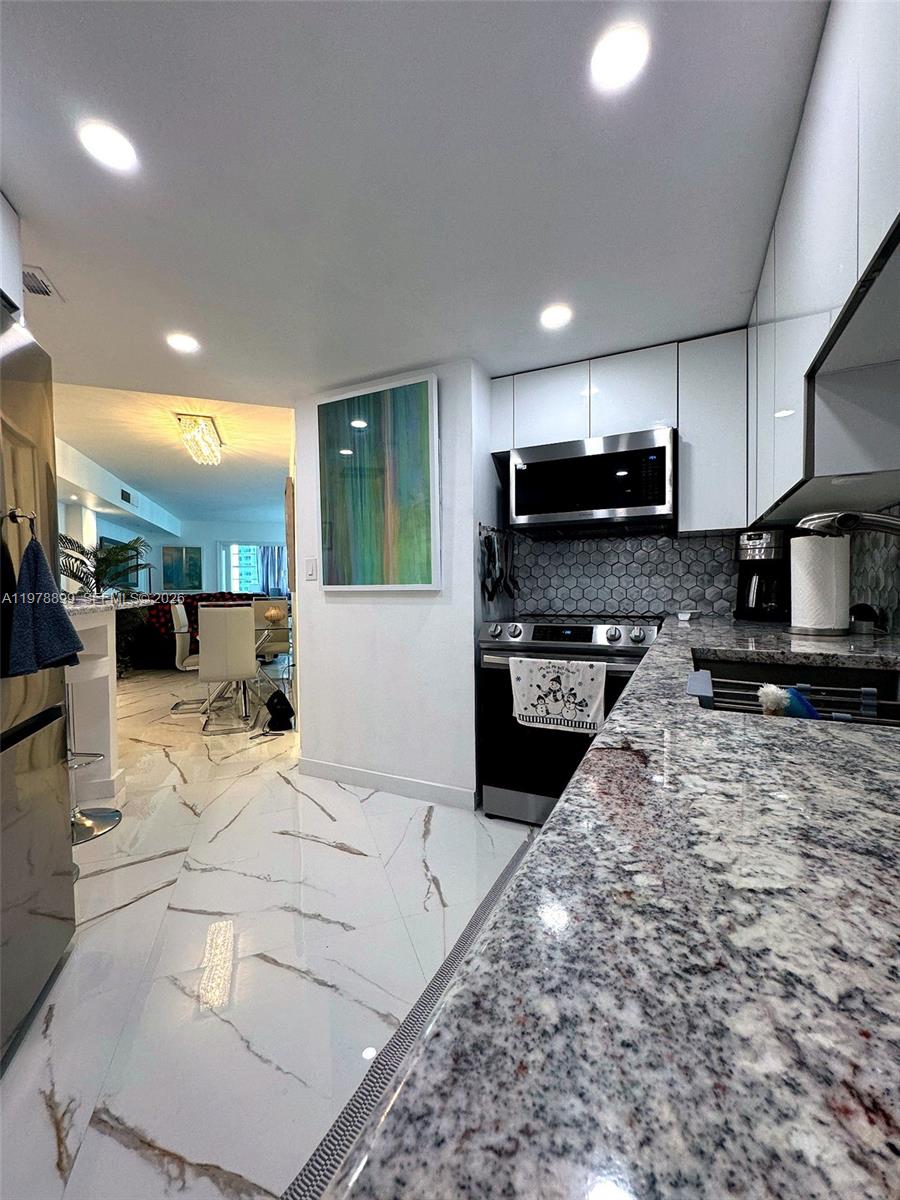 A modern kitchen features granite countertops, white cabinets, and a hexagonal tile backsplash — 999 Brickell Bay Dr # 710, Miami FL 33131, MIAMI, FL