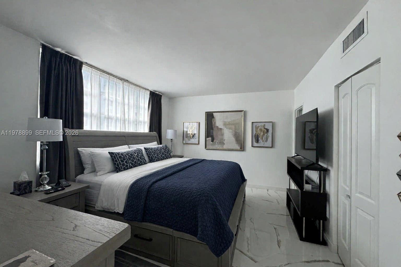 A bedroom features a bed with a navy quilt, marble flooring, and a wall-mounted television — 999 Brickell Bay Dr # 710, Miami FL 33131, MIAMI, FL