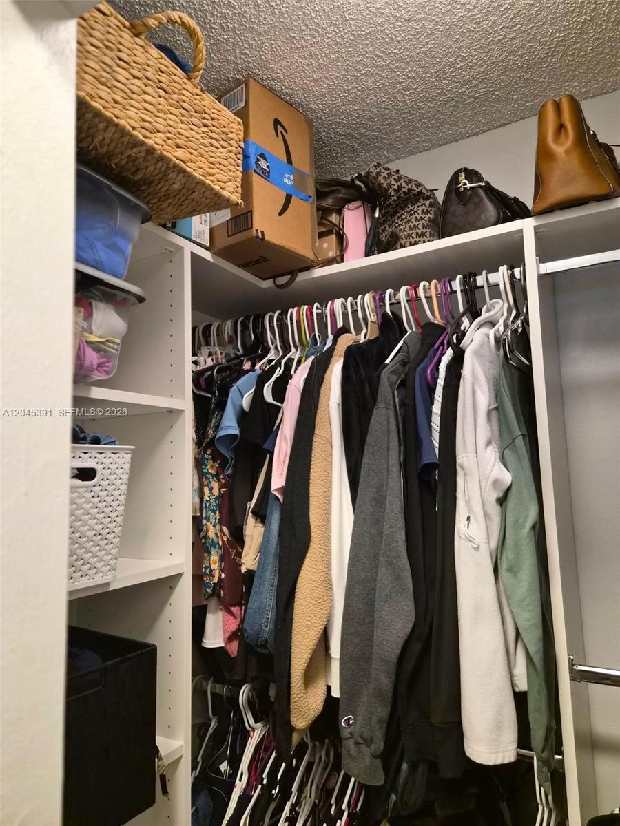 A walk-in closet features white shelving, a hanging rod with clothes, and storage bins — 109 Gardens Dr # 104, Pompano Beach FL 33069, POMPANO BEACH, FL