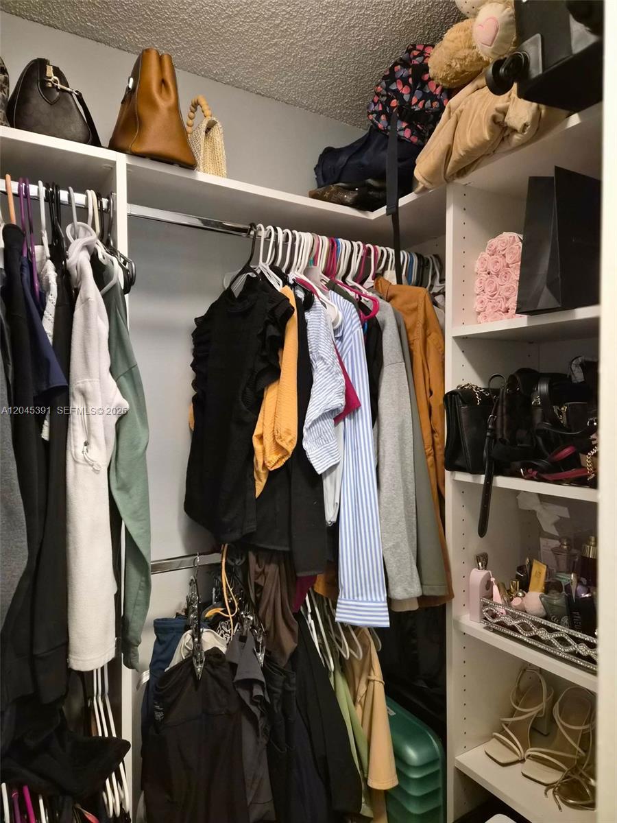 A walk-in closet features white shelving, a hanging rod for clothes, and organized accessories — 109 Gardens Dr # 104, Pompano Beach FL 33069, POMPANO BEACH, FL