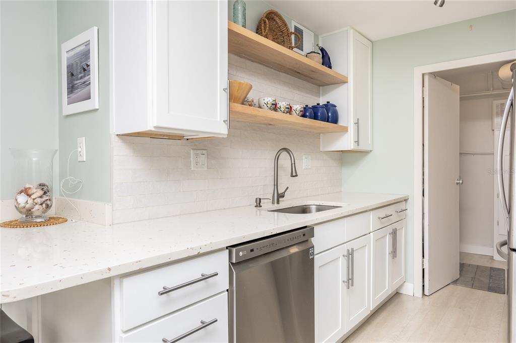 A kitchen features white cabinets, open wood shelving, a stainless steel dishwasher, and quartz countertops — 10355 PARADISE BOULEVARD UNIT 412, ST PETERSBURG, FL