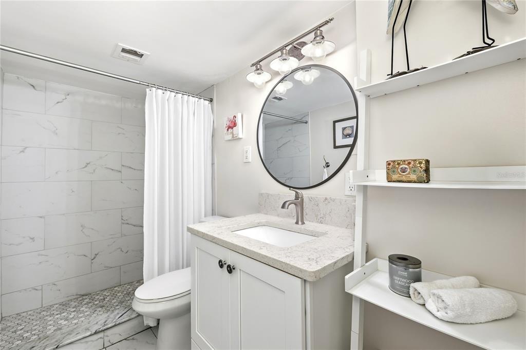 A bathroom features a marble-tiled shower, a white vanity with a stone countertop, and a mirror — 10355 PARADISE BOULEVARD UNIT 412, ST PETERSBURG, FL