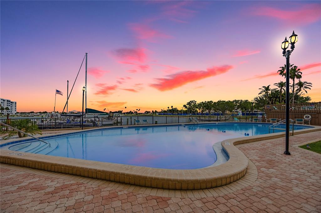 A swimming pool sits on a brick patio overlooking a marina at sunset — 10355 PARADISE BOULEVARD UNIT 412, ST PETERSBURG, FL