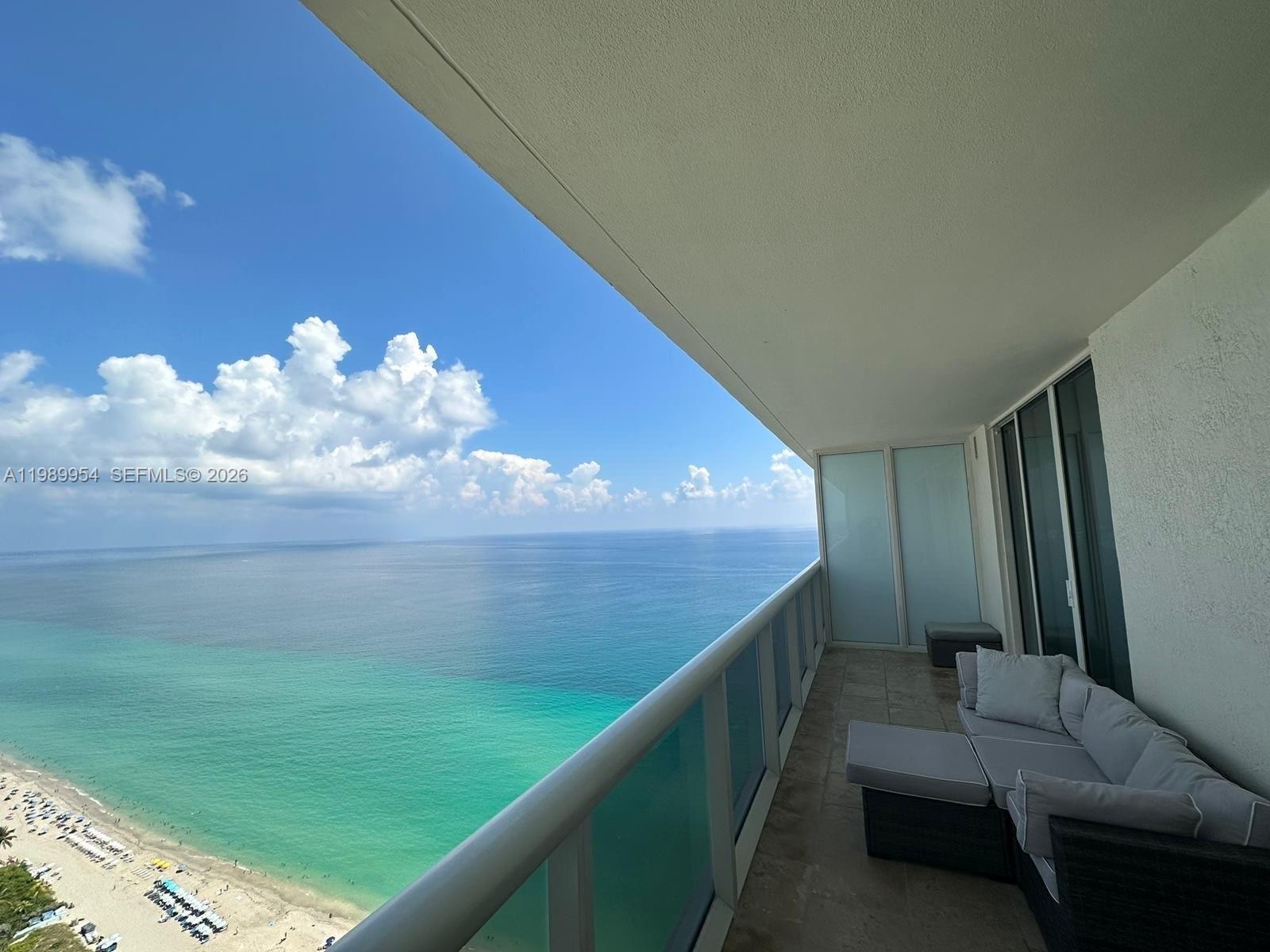 A high-rise balcony features a gray sectional sofa overlooking a sandy beach and ocean — 1830 S Ocean Dr # 4010, Hallandale Beach FL 33009, HALLANDALE BEACH, FL