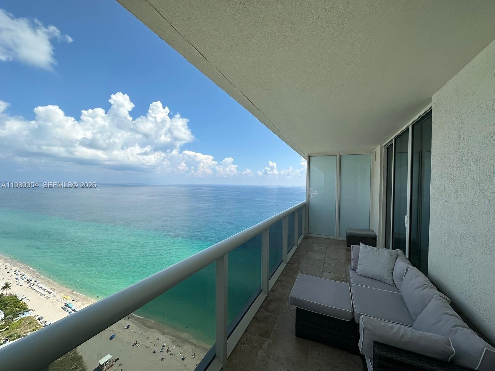 A high-rise balcony features a gray sectional sofa overlooking a sandy beach and ocean — 1830 S Ocean Dr # 4010, Hallandale Beach FL 33009, HALLANDALE BEACH, FL