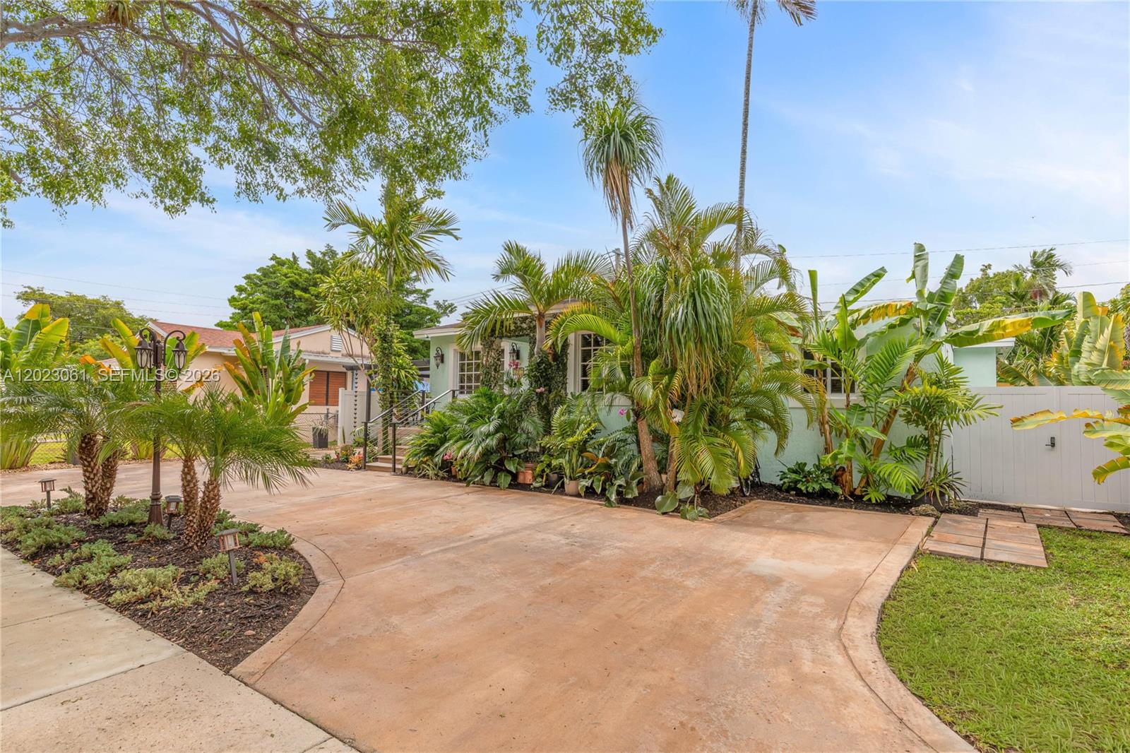 A light green house with a concrete driveway is surrounded by lush tropical landscaping — 6520 SW 16th Ter, West Miami FL 33155, WEST MIAMI, FL