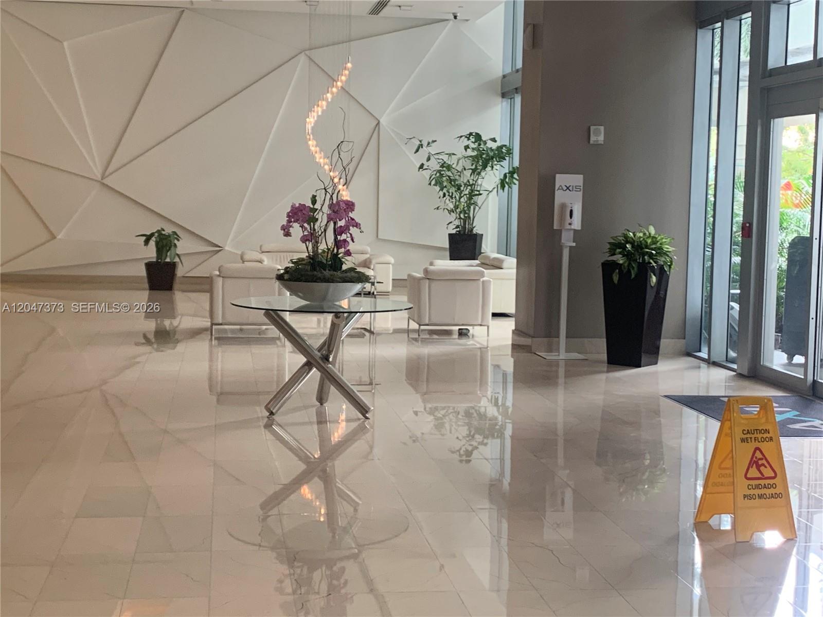 A modern building lobby features white tiled floors, geometric wall panels, and a glass table — 1111 SW 1 AV, Miami FL 33130, MIAMI, FL
