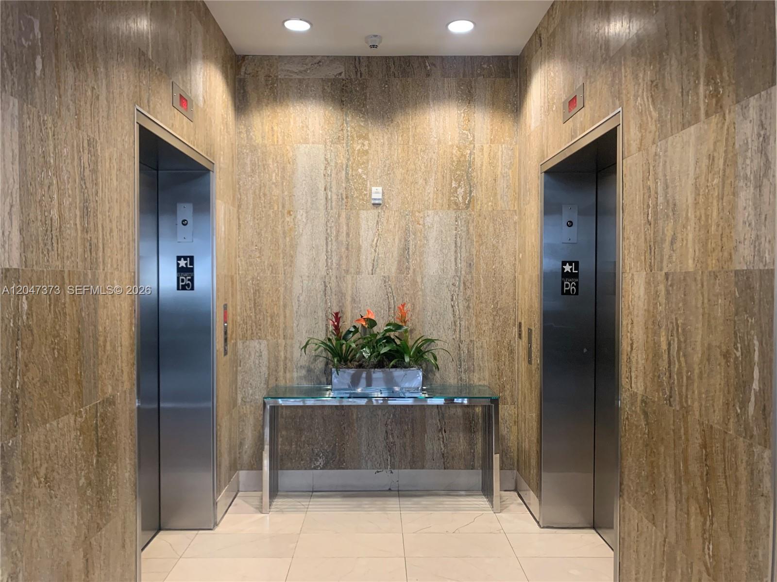 An elevator lobby features two stainless steel elevators, a glass console table, and stone walls — 1111 SW 1 AV, Miami FL 33130, MIAMI, FL