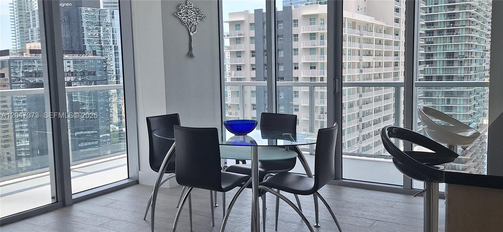 A dining area with a glass table, black chairs, and floor-to-ceiling windows overlooking city buildings — 1111 SW 1 AV, Miami FL 33130, MIAMI, FL