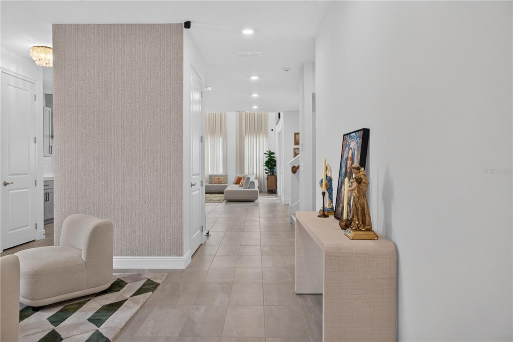 A hallway with tile flooring leads to a living area with tall windows and furniture — 2254 LOST HORIZON WAY, MINNEOLA, FL