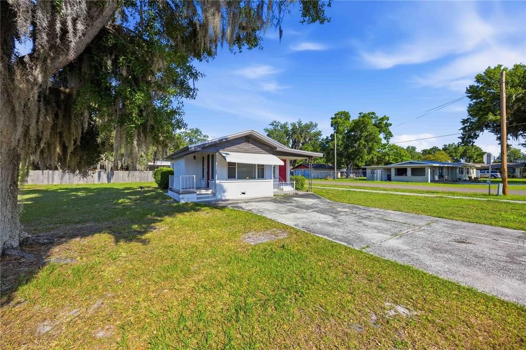 A small, white, single-story house with a concrete driveway and a large tree in front — 1997 26TH STREET NW, WINTER HAVEN, FL