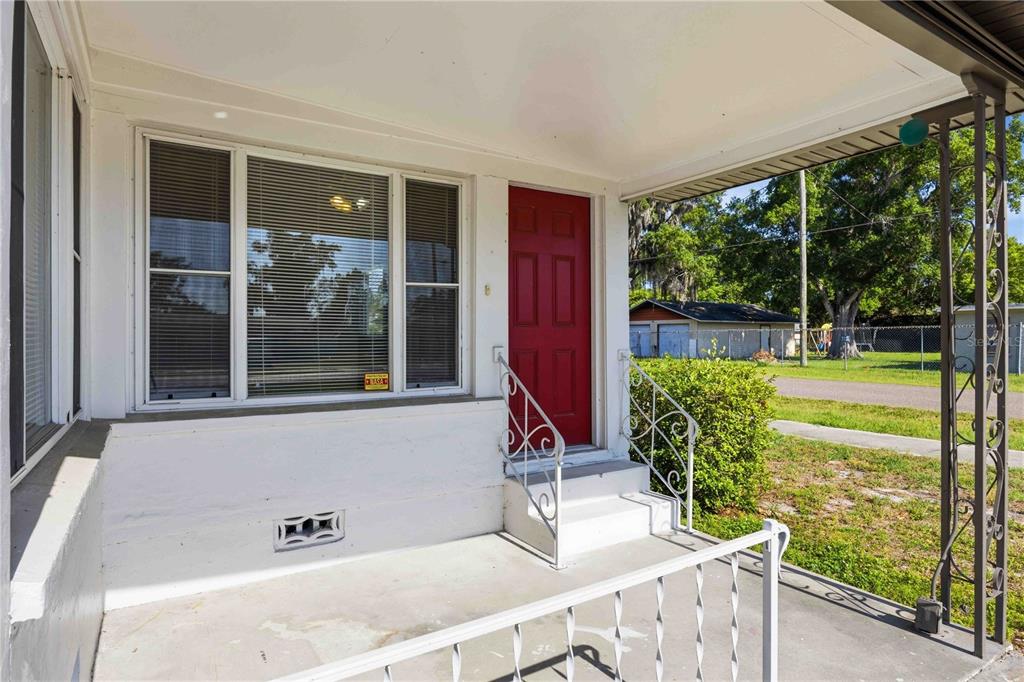 A white concrete porch features a red front door, white metal railings, and large windows — 1997 26TH STREET NW, WINTER HAVEN, FL