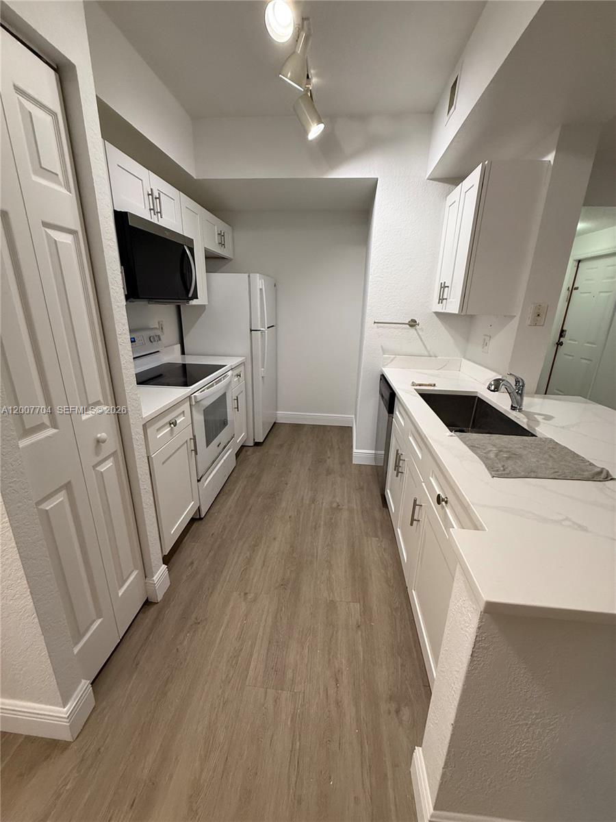 A galley-style kitchen features white cabinets, stainless steel appliances, and light wood-look flooring — 2500 Centergate Dr # 104, Miramar FL 33025, MIRAMAR, FL