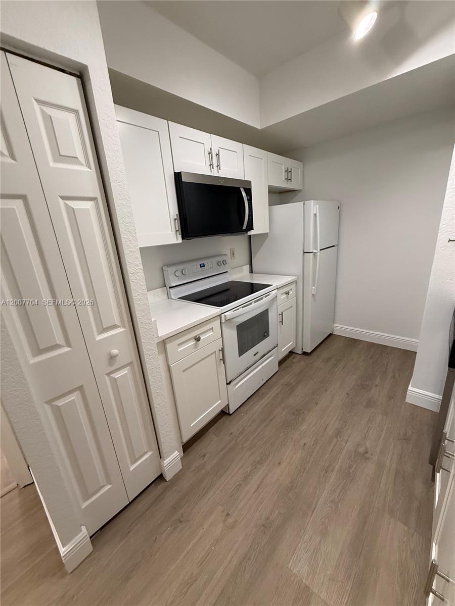 A kitchen features white cabinets, stainless steel appliances, and light wood-look flooring — 2500 Centergate Dr # 104, Miramar FL 33025, MIRAMAR, FL