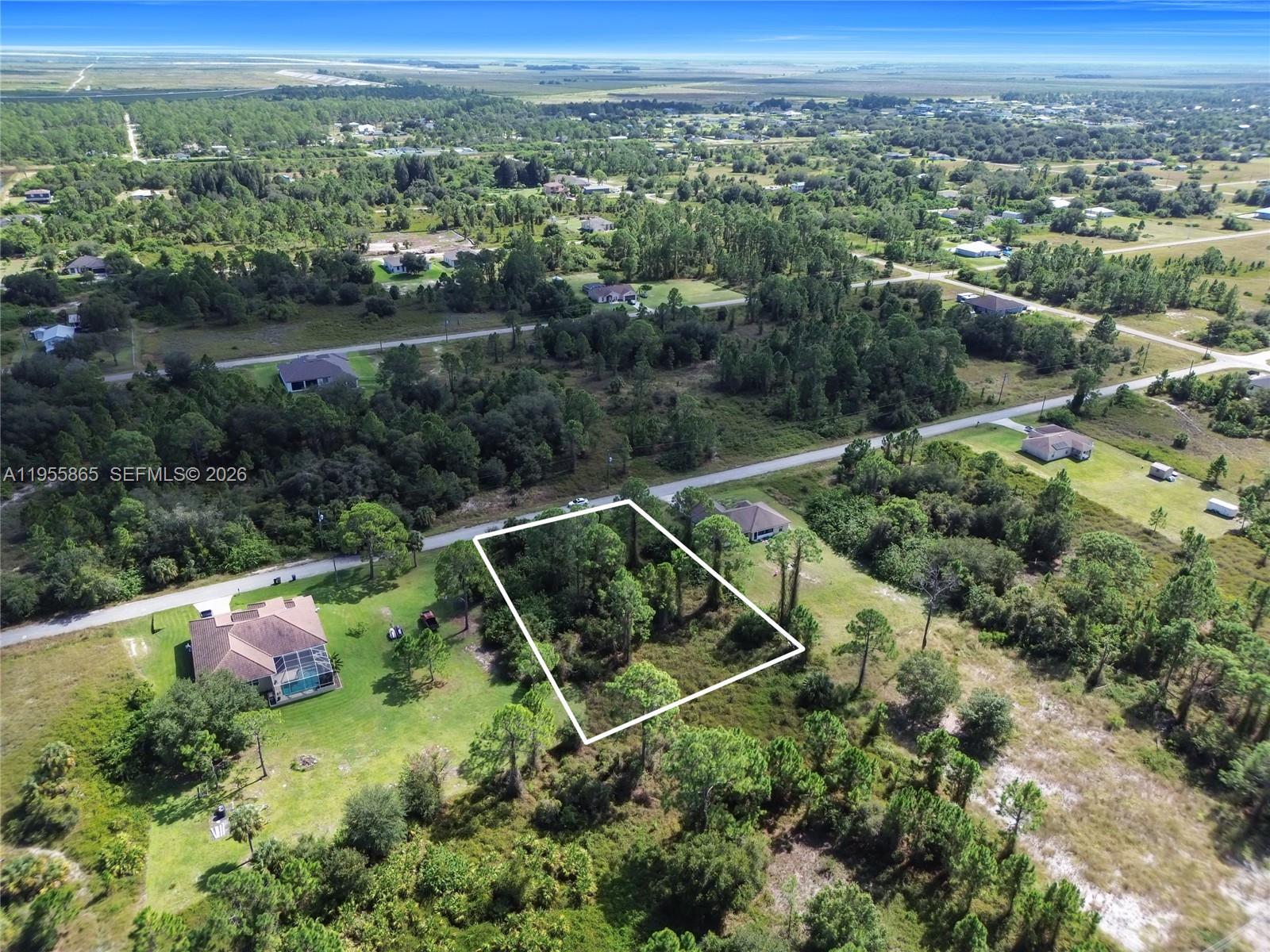 An aerial view shows a rectangular vacant lot outlined in white amidst a wooded area — 1915 Louis Ave, Lehigh Acres FL 33972, LEHIGH ACRES, FL
