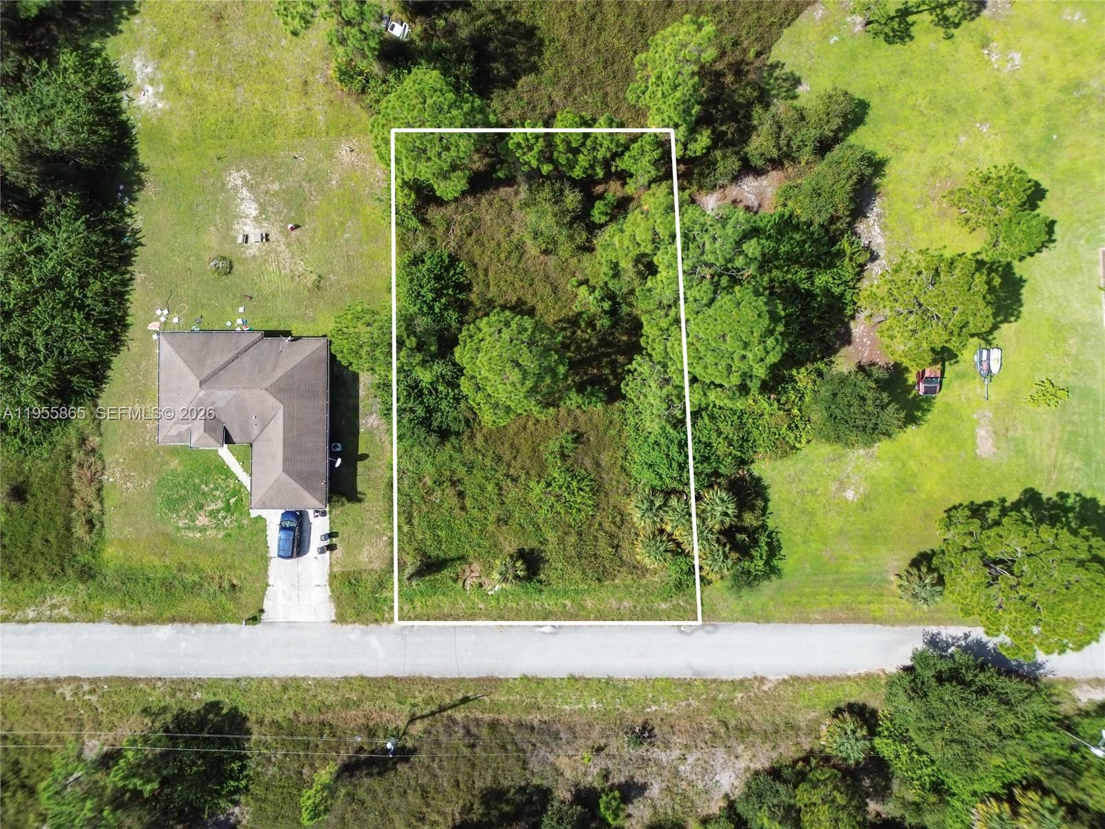 An aerial view shows a rectangular vacant lot bordered by a road and trees — 1915 Louis Ave, Lehigh Acres FL 33972, LEHIGH ACRES, FL