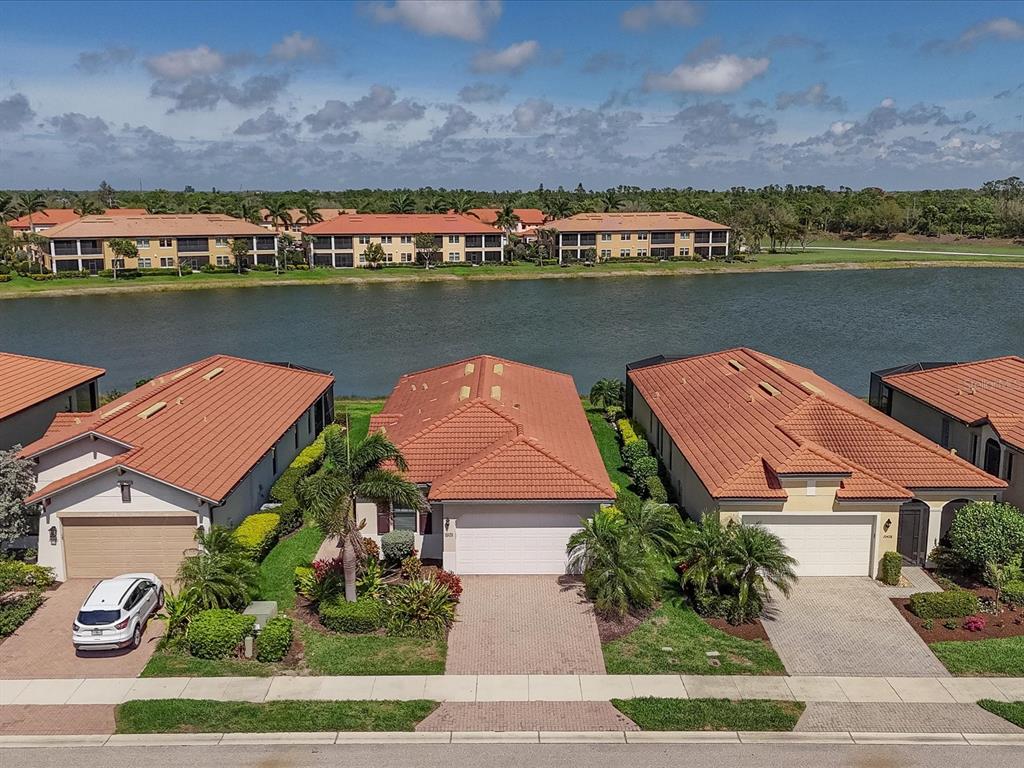 An aerial view shows three suburban houses with terracotta roofs facing a lake — 10424 CROOKED CREEK DRIVE, VENICE, FL