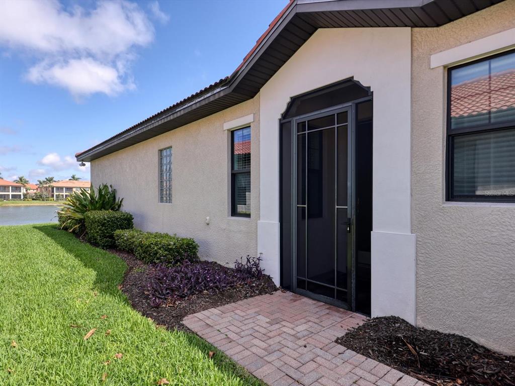 A side view of a house exterior featuring a brick walkway, screen door, and landscaping — 10424 CROOKED CREEK DRIVE, VENICE, FL