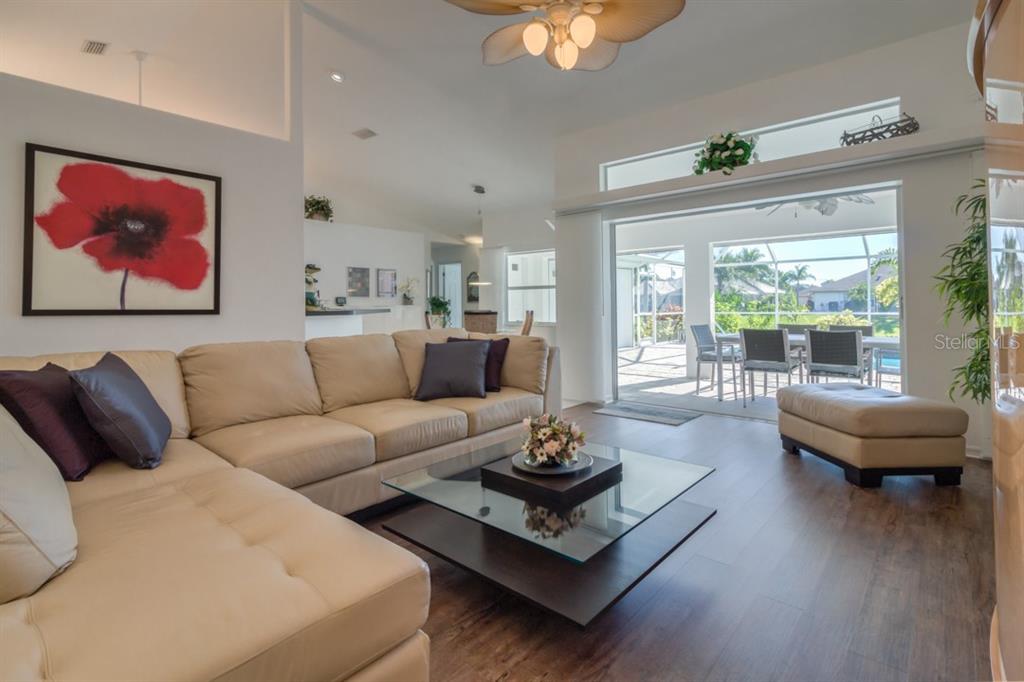 A living room features a beige sectional sofa, a glass coffee table, and sliding glass doors — 26 LONG MEADOW LANE, ROTONDA WEST, FL