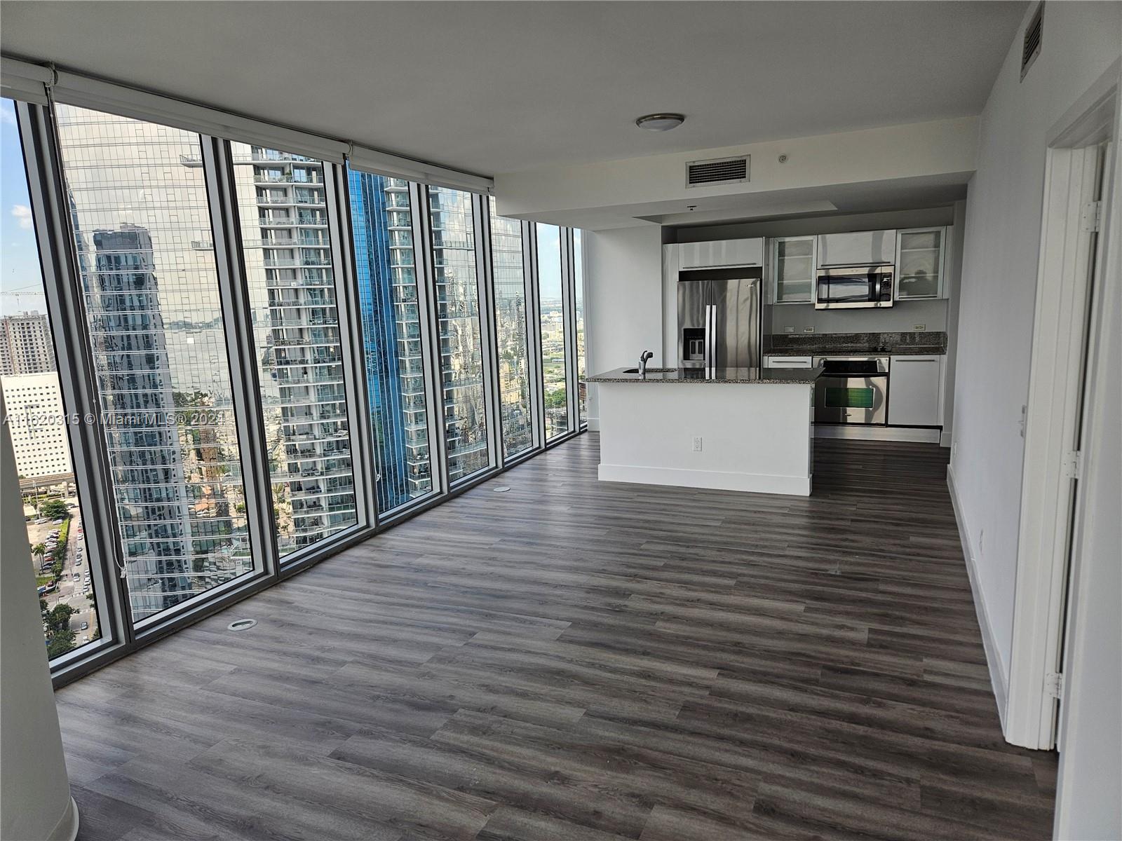 An open-concept kitchen and living area features floor-to-ceiling windows and wood-look flooring — 888 Biscayne Blvd # 4001, Miami FL 33132, MIAMI, FL