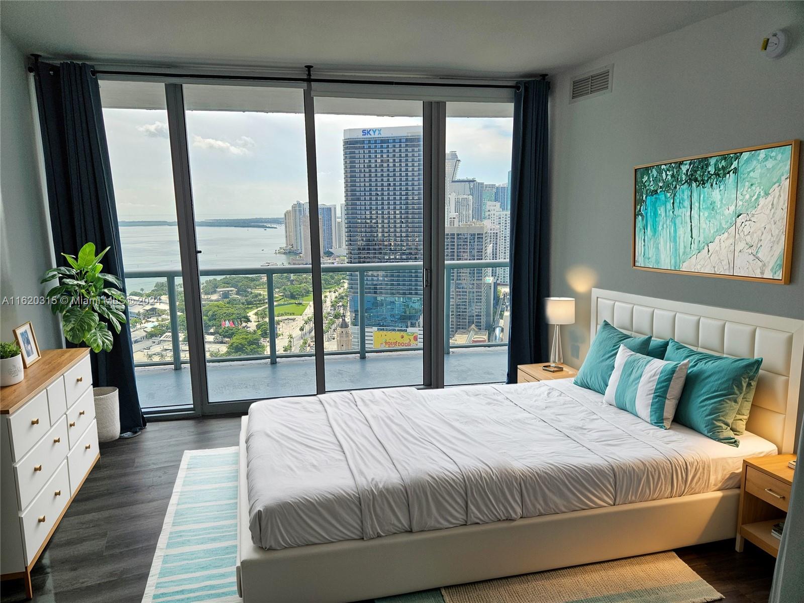 A bedroom features a white bed, a dresser, and floor-to-ceiling windows overlooking a city skyline — 888 Biscayne Blvd # 4001, Miami FL 33132, MIAMI, FL