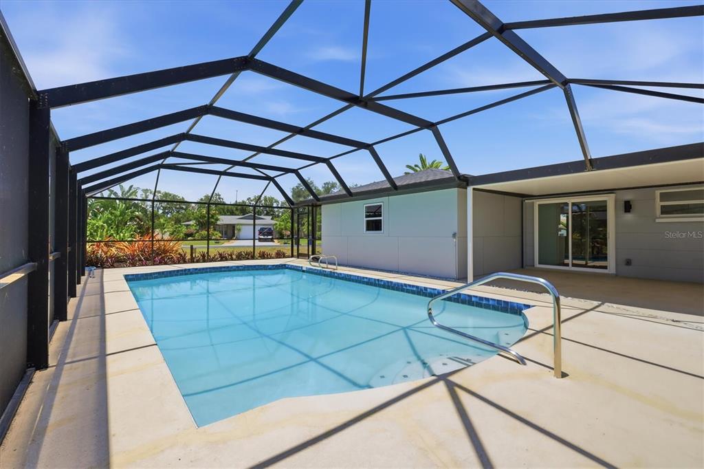 A swimming pool with a screened-in enclosure sits on a concrete patio behind a house — 1600 CYPRESS POINT COURT, VENICE, FL