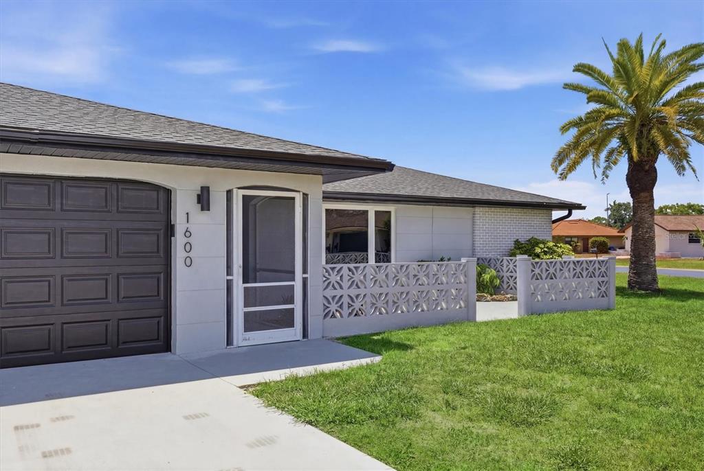 A single-story house exterior features a dark garage door, a screen door, and decorative masonry walls — 1600 CYPRESS POINT COURT, VENICE, FL